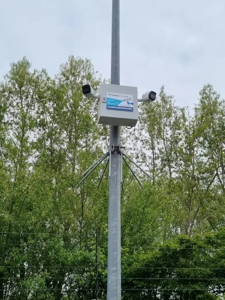 Aansluitkast en camera samen op een paal, direct achter een stalen hekwerk