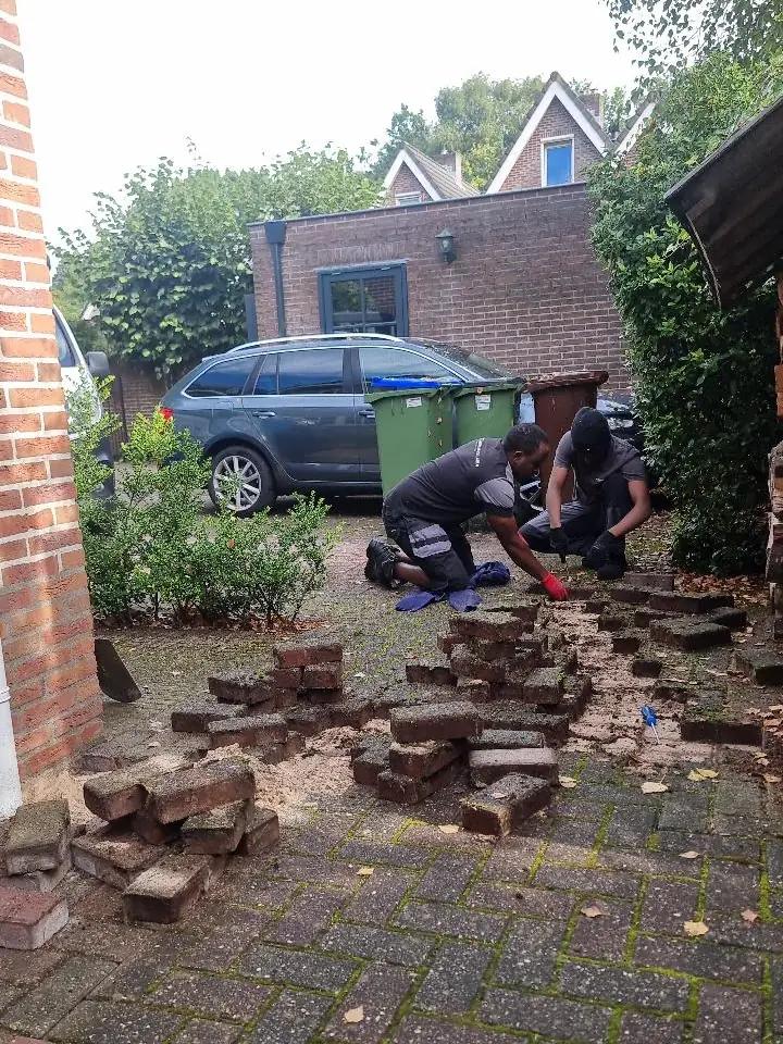 De klinkers gaan opzij zodat de sleuf naar de paal gegraven kan worden
