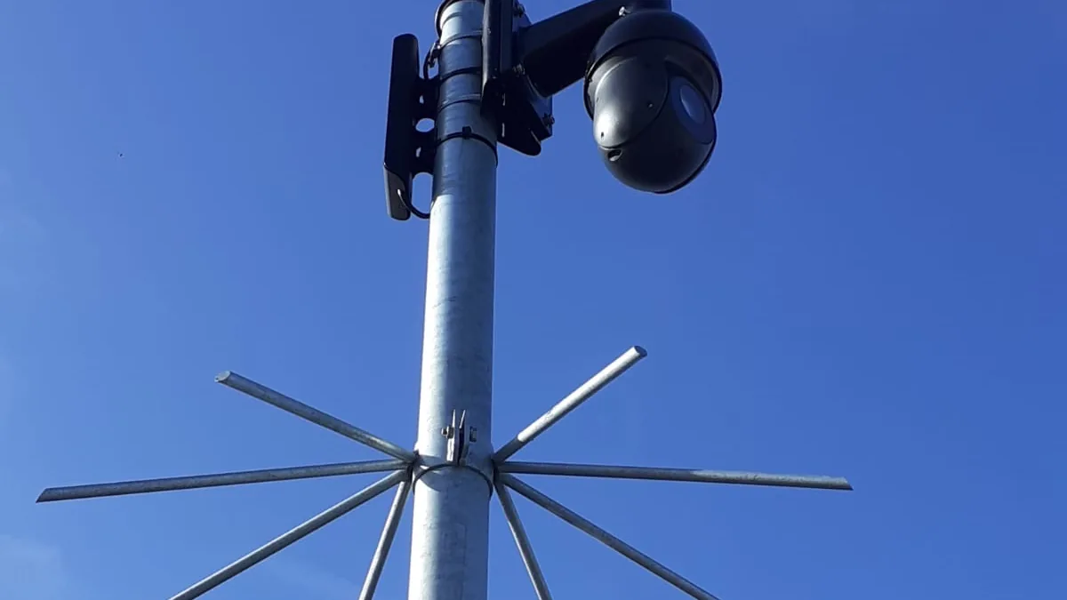 Verzinkte camerapaal met een draaibare camera bovenop, tegen een strakblauwe lucht