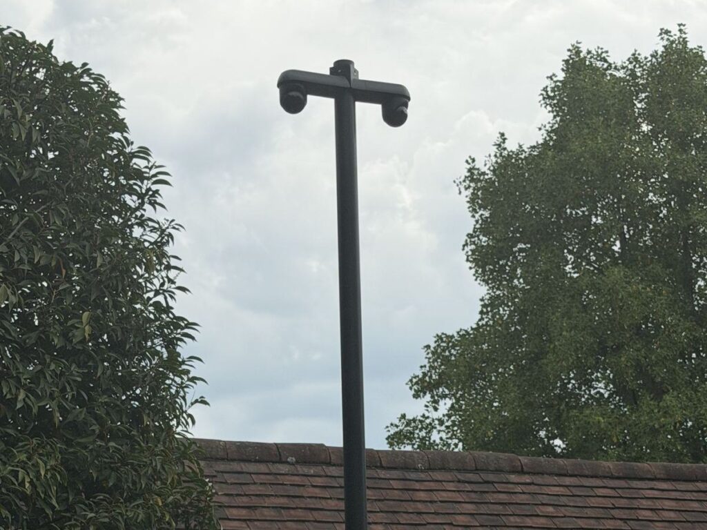 Camerapaal met een dwarsarm en twee camera's, ruim boven een pannendak uit