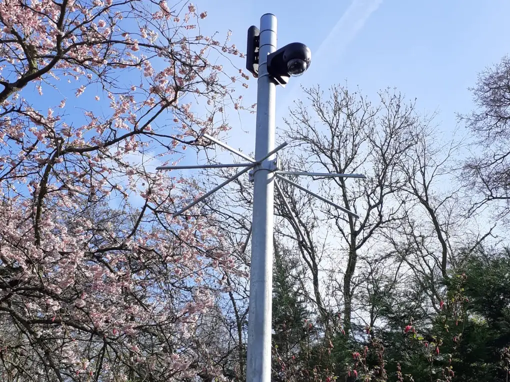 Camerapaal tussen bloeiende bomen op een erf