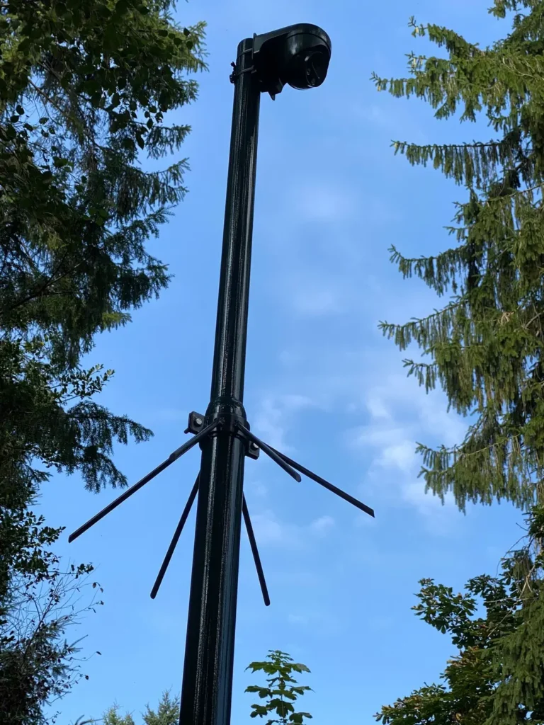 Zwarte camerapaal tussen de bomen met een draaibare camera bovenin