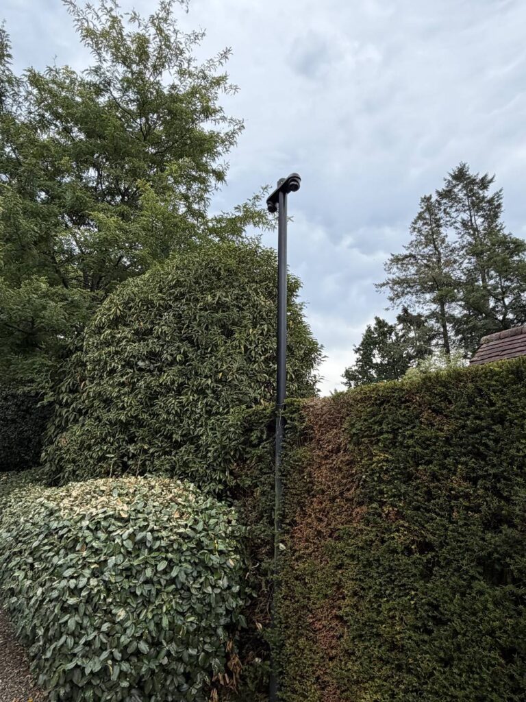 Zwarte camerapaal die tussen de hagen van een aangelegde tuin wegvalt