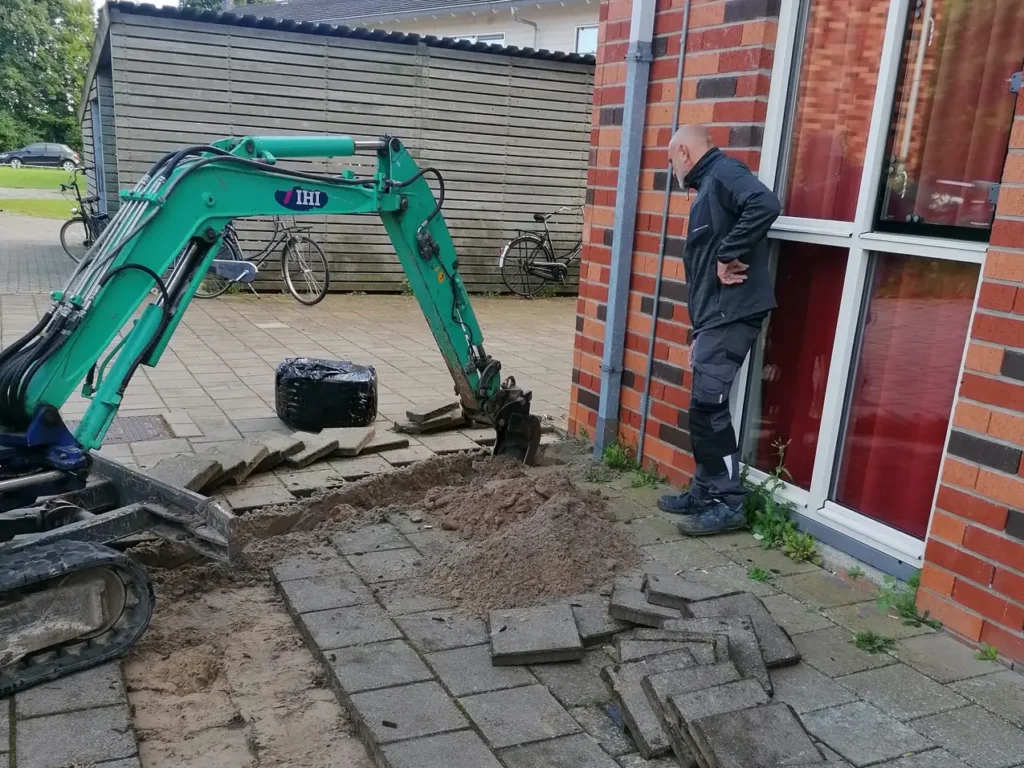 Graafwerk langs de woning met een minigraver, de bestrating tijdelijk opzij