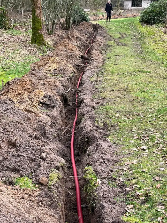 Lange sleuf door het gras met de mantelbuis er al in, klaar om dicht te gaan
