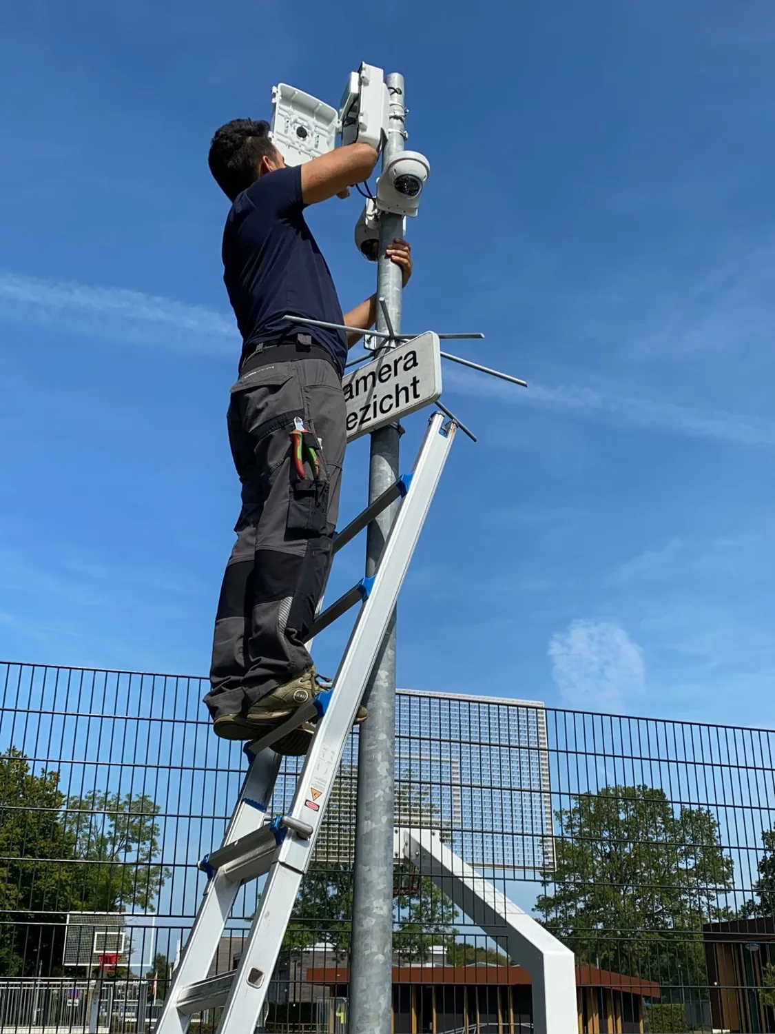 Monteur monteert een camera op een paal langs het hekwerk