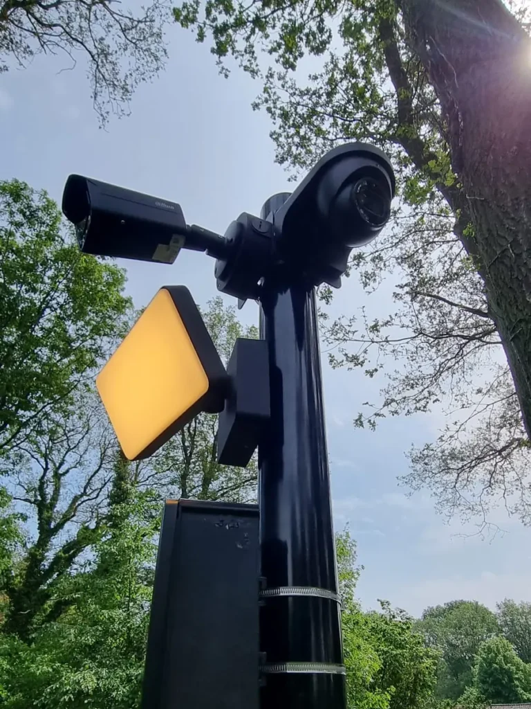 Monteur aan het werk aan een camerapaal in een tuin, met gereedschap op de grond