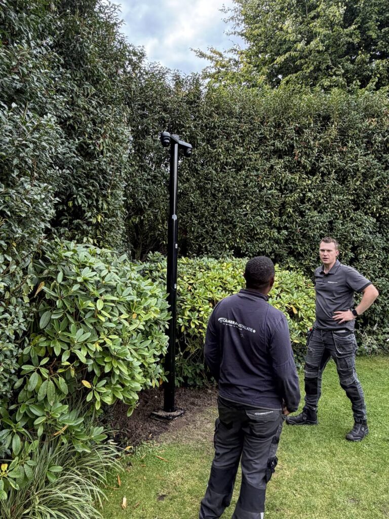 Twee monteurs bij de geplaatste camerapaal in de tuin, met de haag erachter