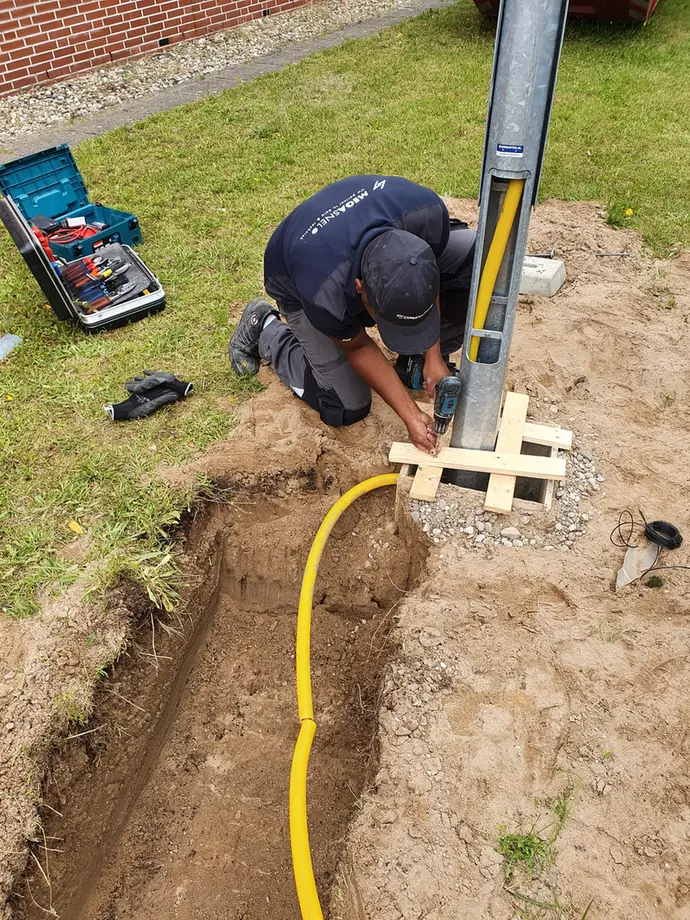 De paal wordt waterpas gesteld boven de open sleuf, met de kabel er al in
