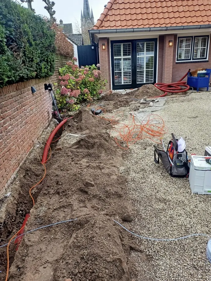 Sleuf dwars door de tuin met mantelbuis en kabel, klaar om dicht te gaan