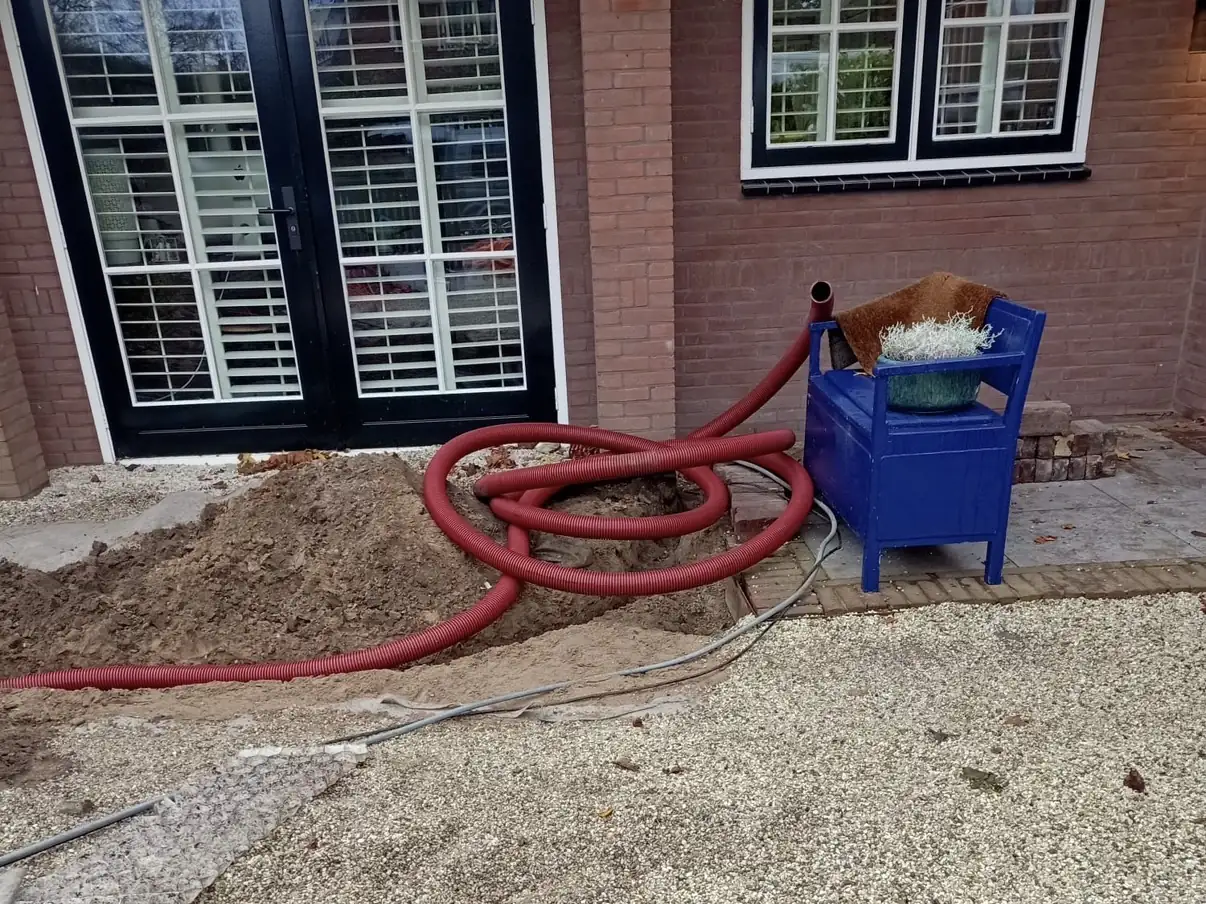 Open sleuf langs de gevel met de mantelbuis er al in, bestrating tijdelijk opzij