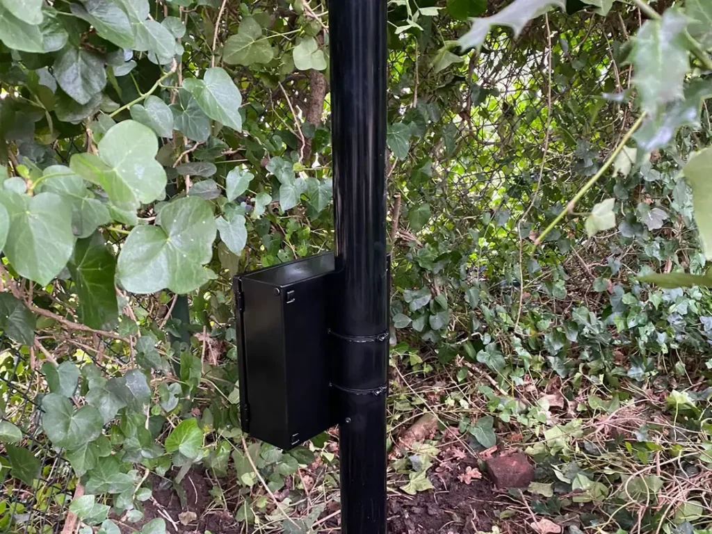 De voet van een camerapaal in de grond, met de kabelinvoer onderaan