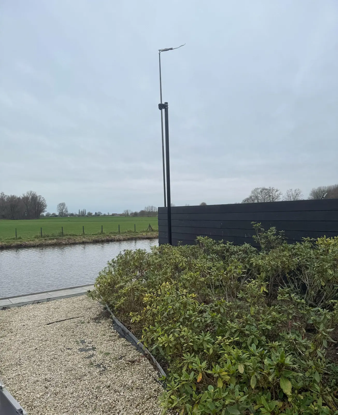 Zwarte cameramast van 4,5 meter achter in een tuin aan het water